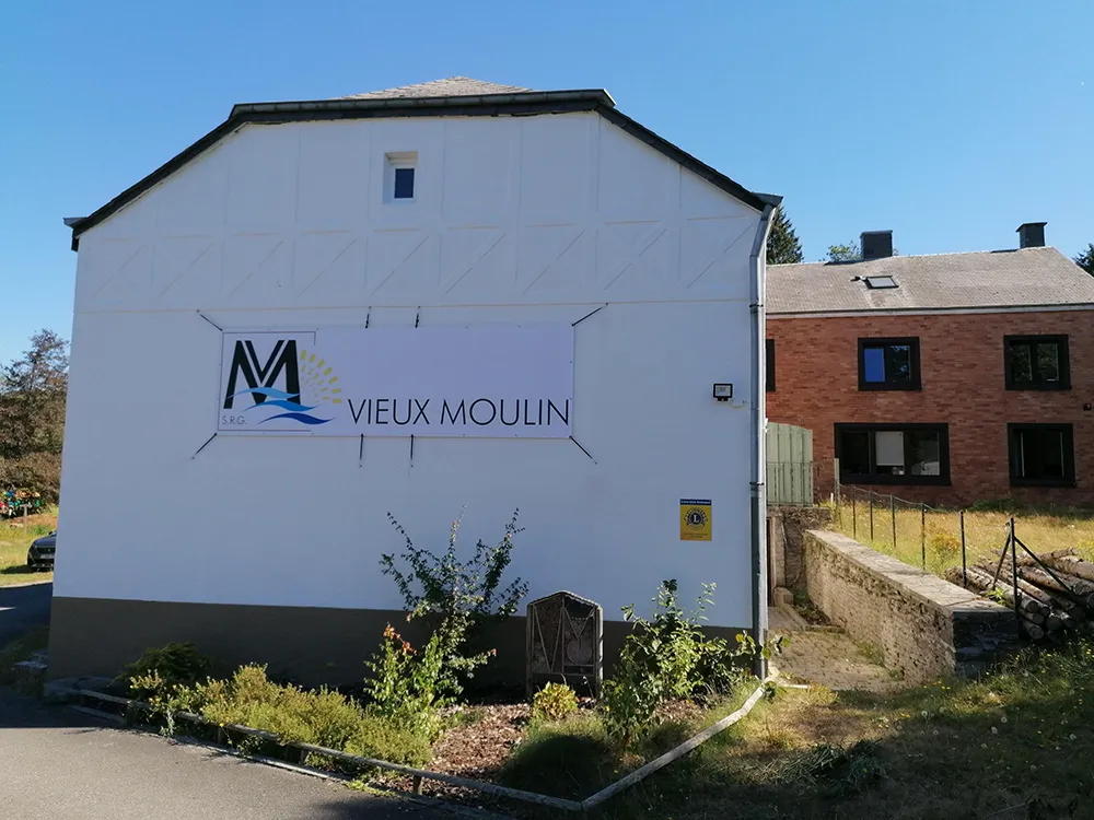 Vue sur la face avant du Vieux Moulin. Il y a une banderole avec le logo du Vieux Moulin dessus.