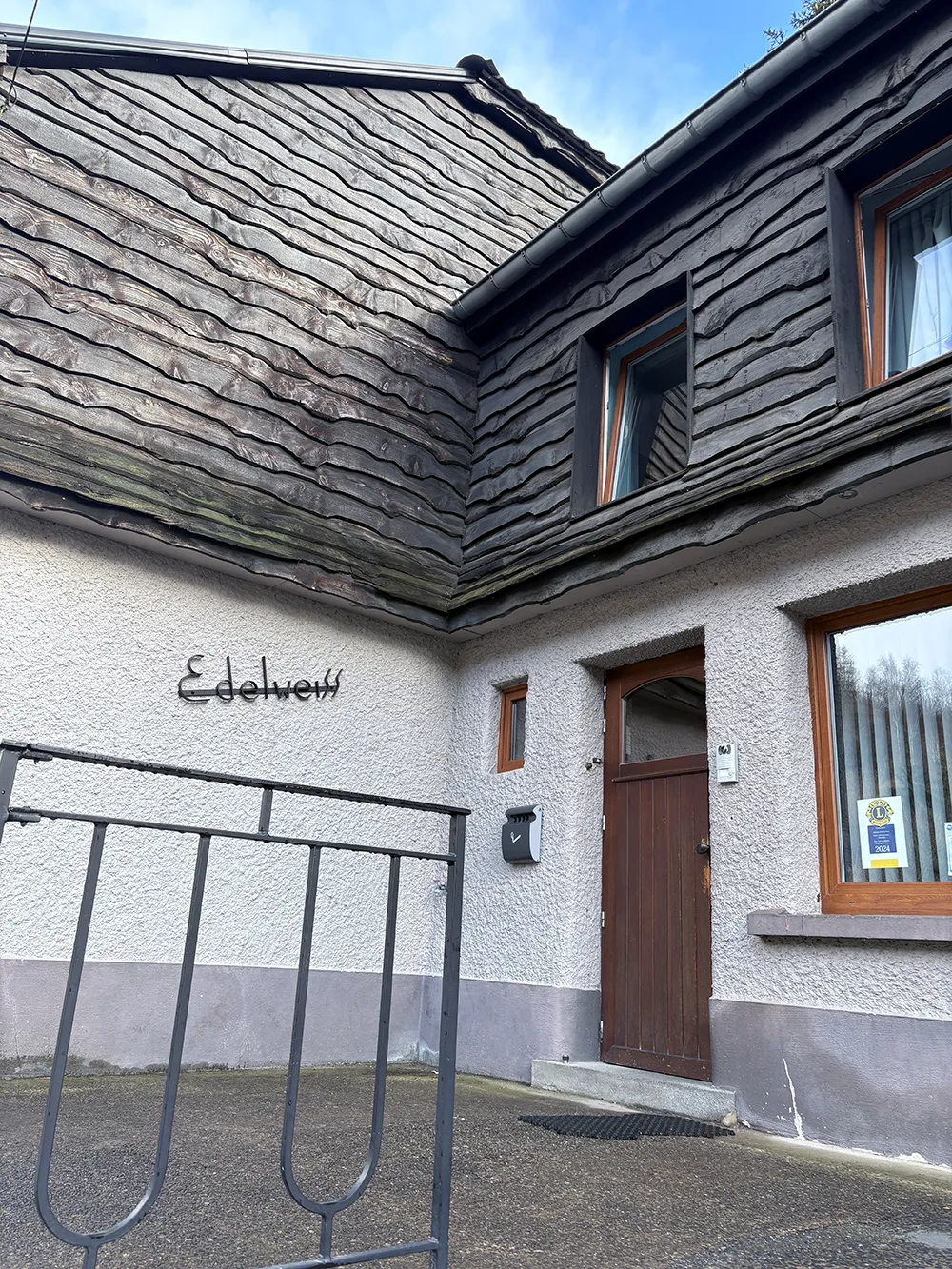 Vue sur la porte d'entrée du foyer l'Edelweiss. Le bâtiment est en bois et en pierre.